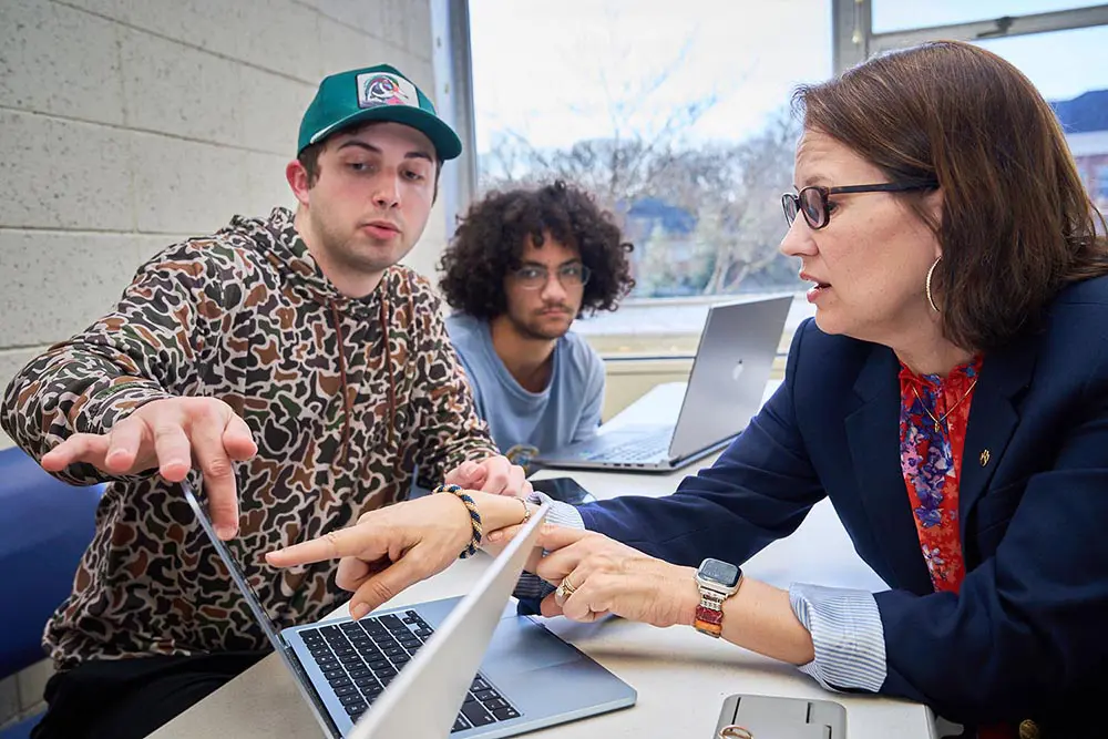 A woman and two male students work on a computer.