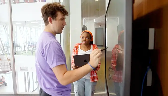 Man working at interactive board while woman in background watches.