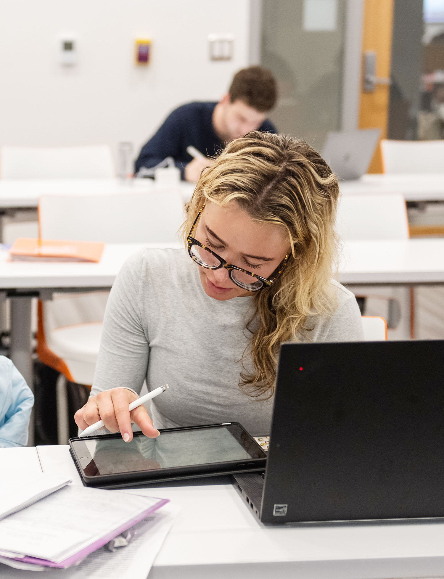 Student in classroom working on iPad with computer in front of her.