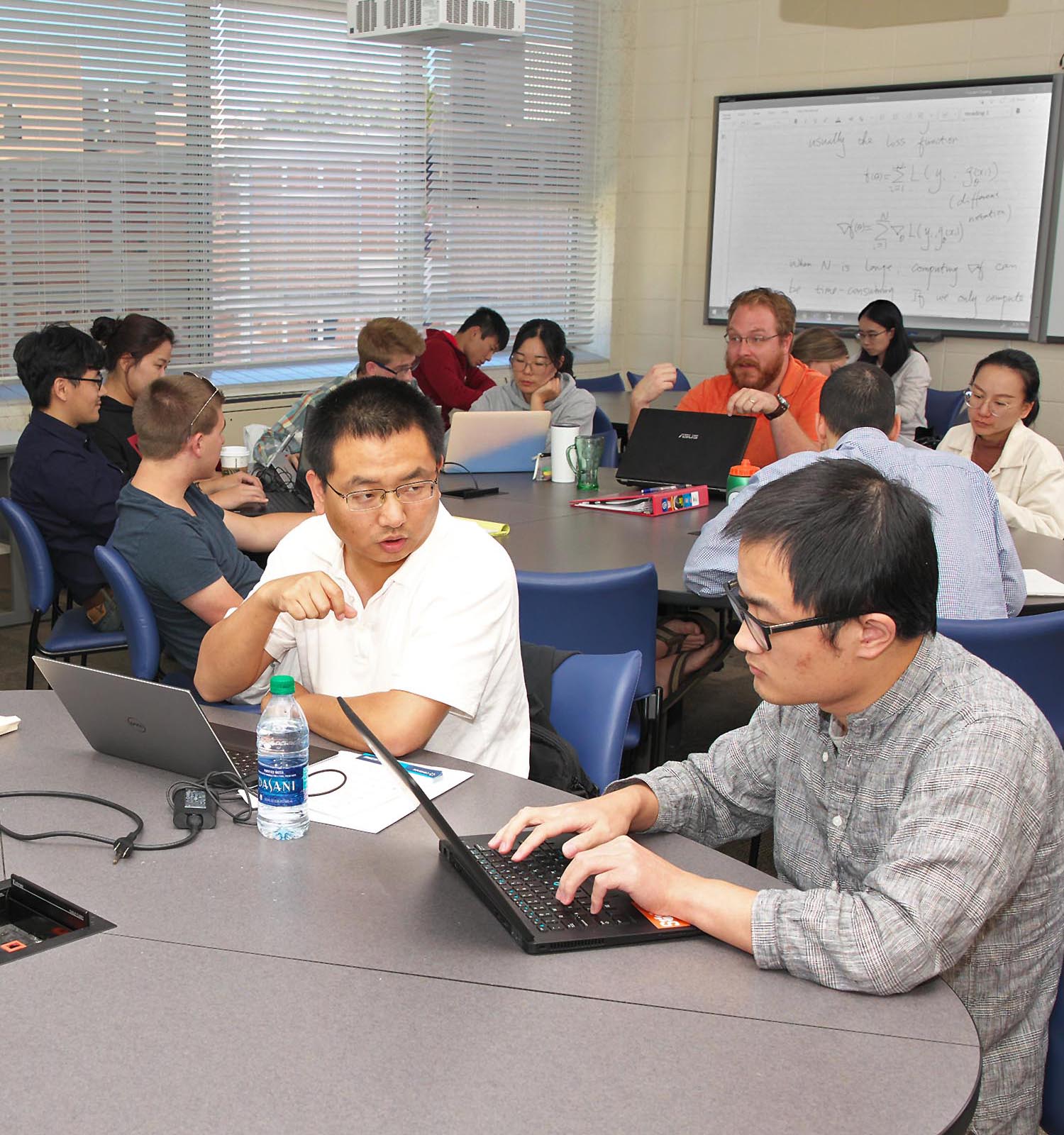 Students working on computers in a math classroom with round tables.