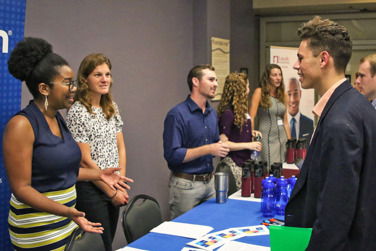 People behind a table at an expo greeting visitors.