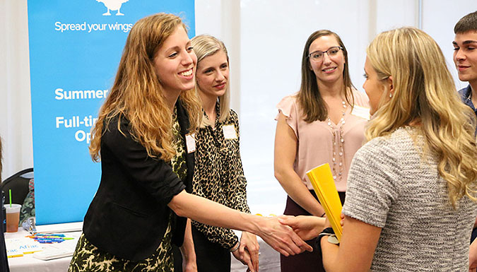 Five people at a conference, shaking hands.