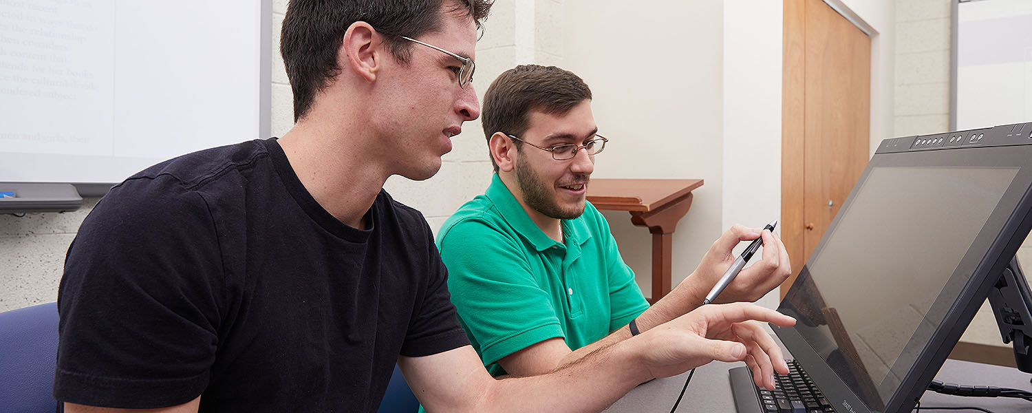 Two male students working on a touchscreen computer in a math lab.