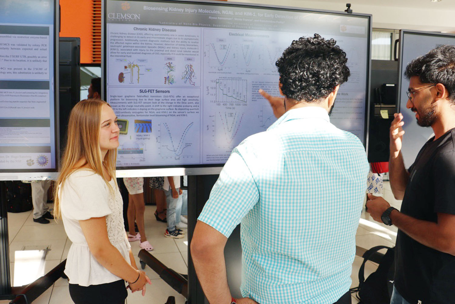 Three people looking at a video display of a science poster presentation.