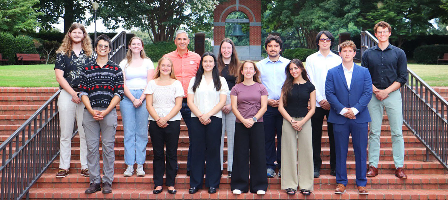 Group of people standing on steps with foliage in the background.