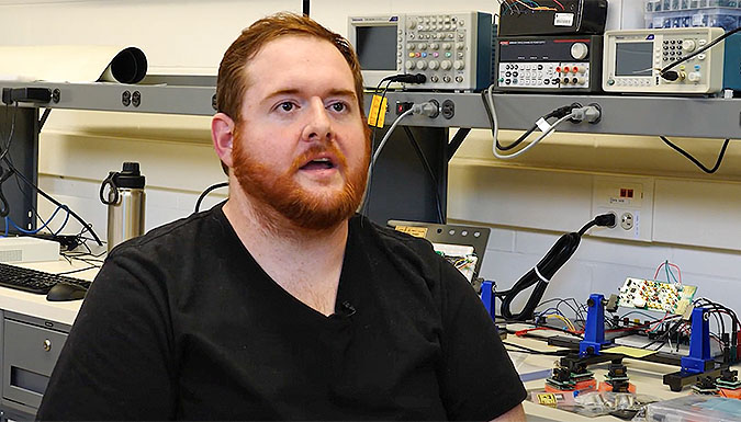 Student in black shirt talking to camera while in science lab.