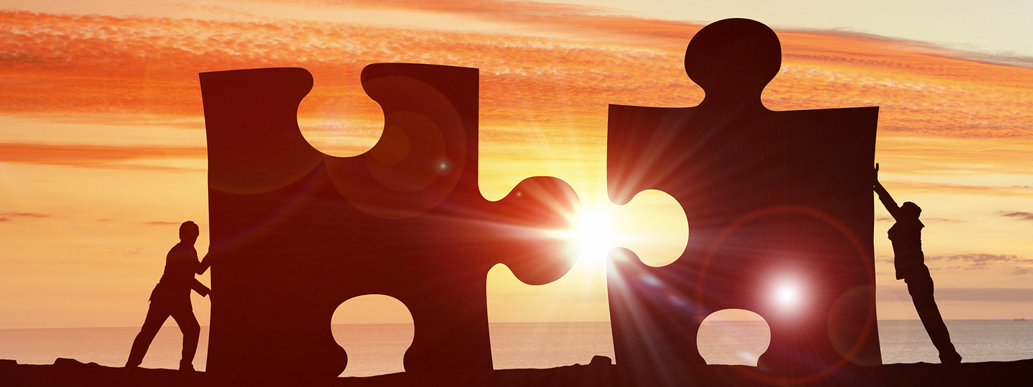 Decorative image of two people pushing large jigsaw pieces in sunset