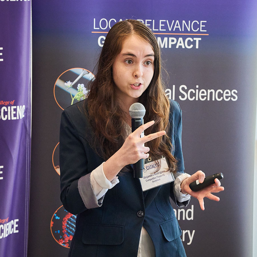 Girl giving presentation in front of a step-and-repeat with the College of Science logo.