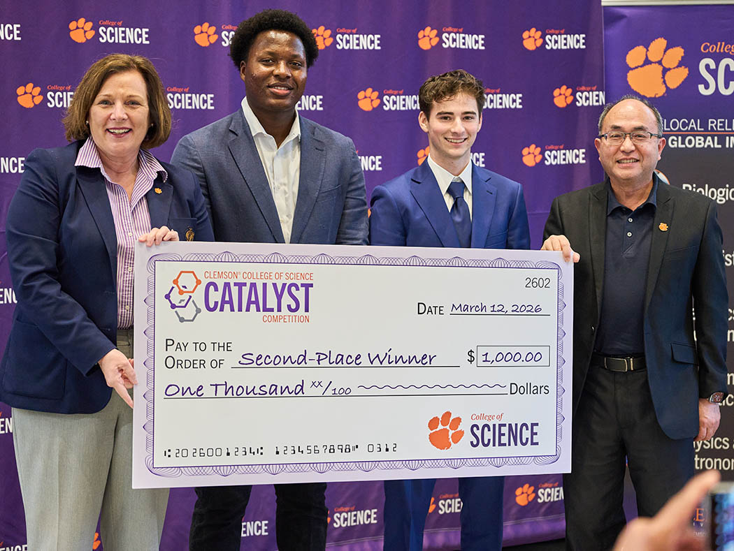 Four people in front of a College of Science purple step-and-repeat wall, holding Catalyst second-place-winner check for $1,000.