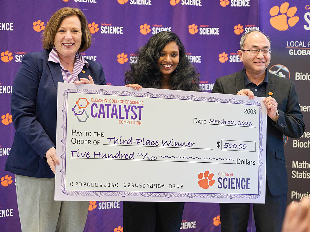 Three people in front of a College of Science purple step-and-repeat wall, holding Catalyst third-place-winner check for $500.