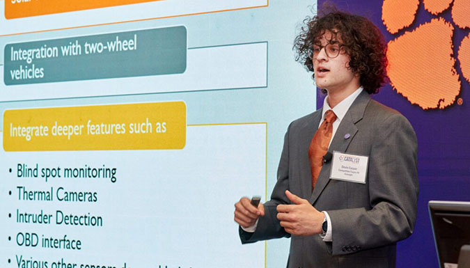Male student presenting in front of a video wall.
