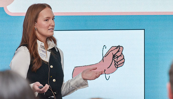 Female student presenting in front of a video wall.