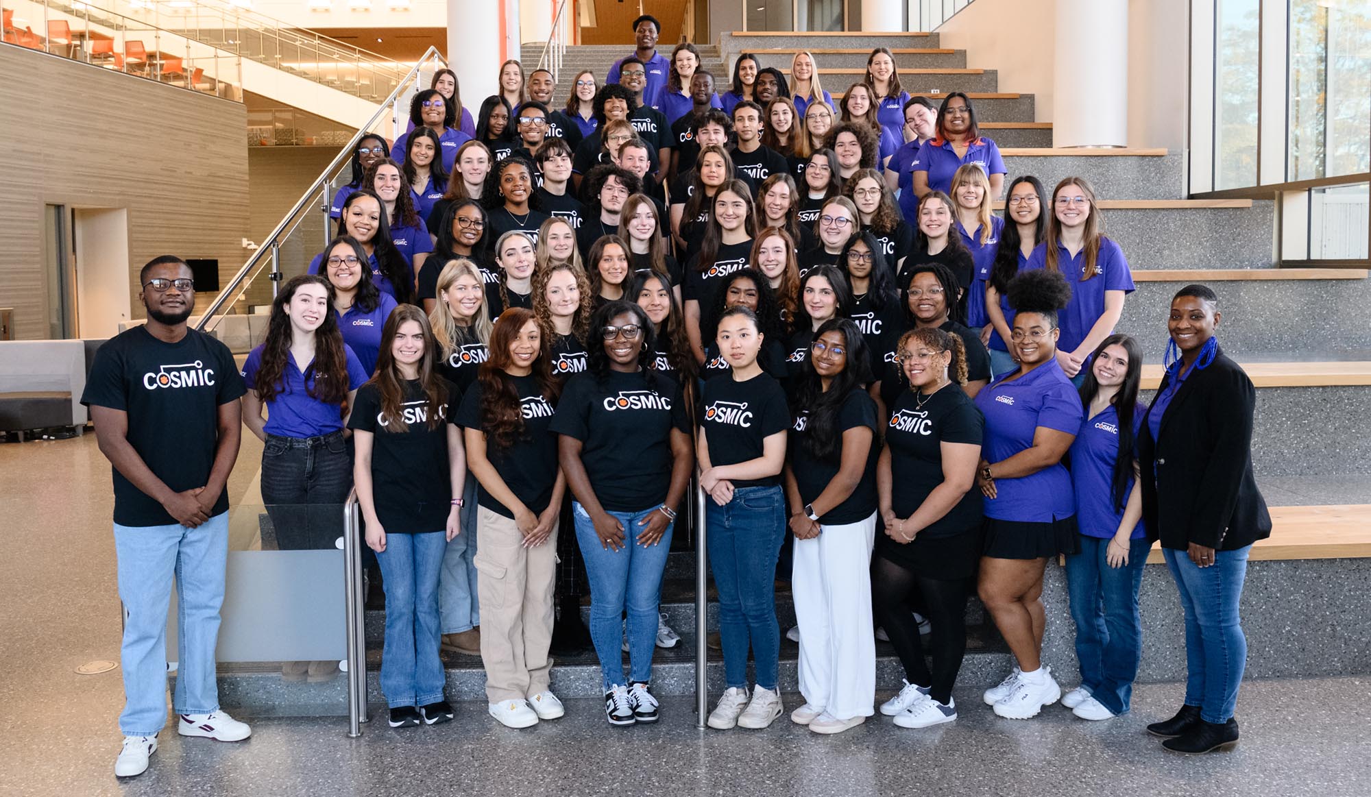 Group of COSMIC mentoring students standing on a staircase, wearing purple shirts.