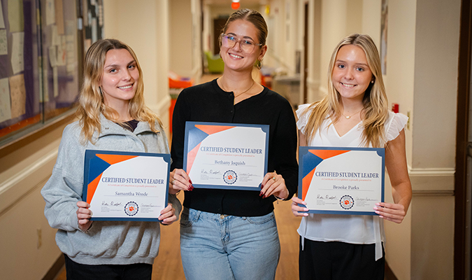 Three females pose for the camera holding Certified Student Leader course completion certificates