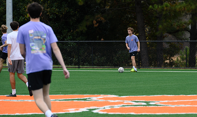 A male student gets ready to kick a soccer ball on a turf playing surface with an orange Tiger Paw on it