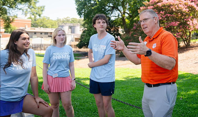 A male in an orange Clemson polo shirt speaks to students