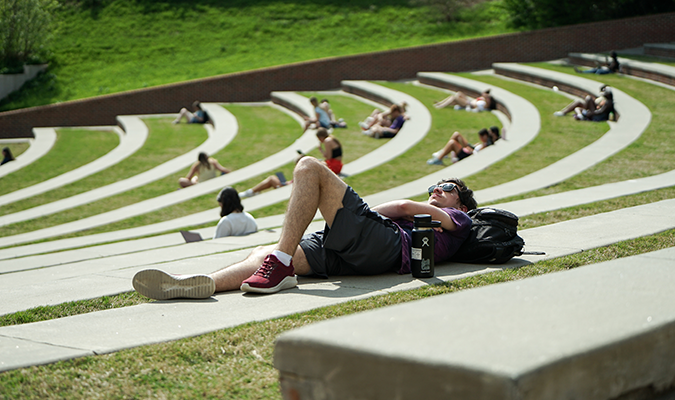 student laying down in the sun at the amphitheater