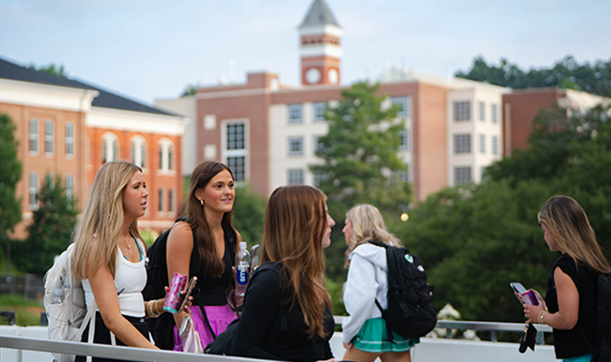 Clemson students walking on the Library Bridge with Old Main Clock Tower visible in the background