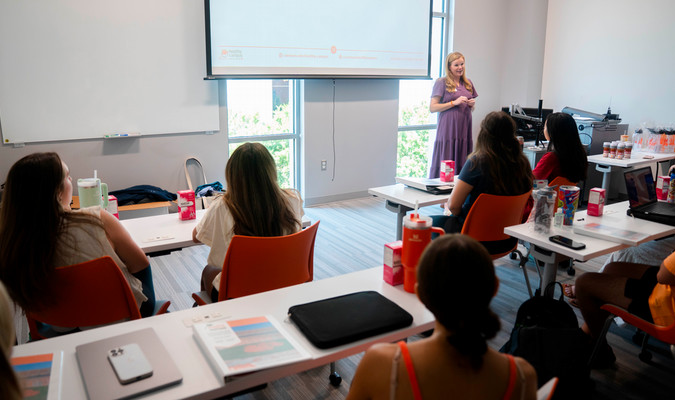 A woman stands in front of a group of people sitting in a classroom setting