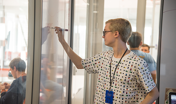 Student writing code on whiteboard at CU HackIt Hackathon