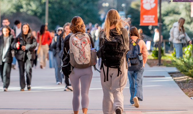 a crowd of students walk on the sidewalk between the Humanities building