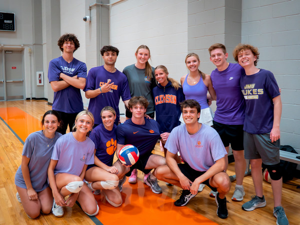 Group of students in purple shirts pose on an indoor gym court, with one holding a volleyball.
