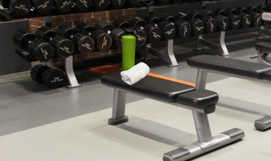 water bottle sitting by a weight bench with dumbbells in the background