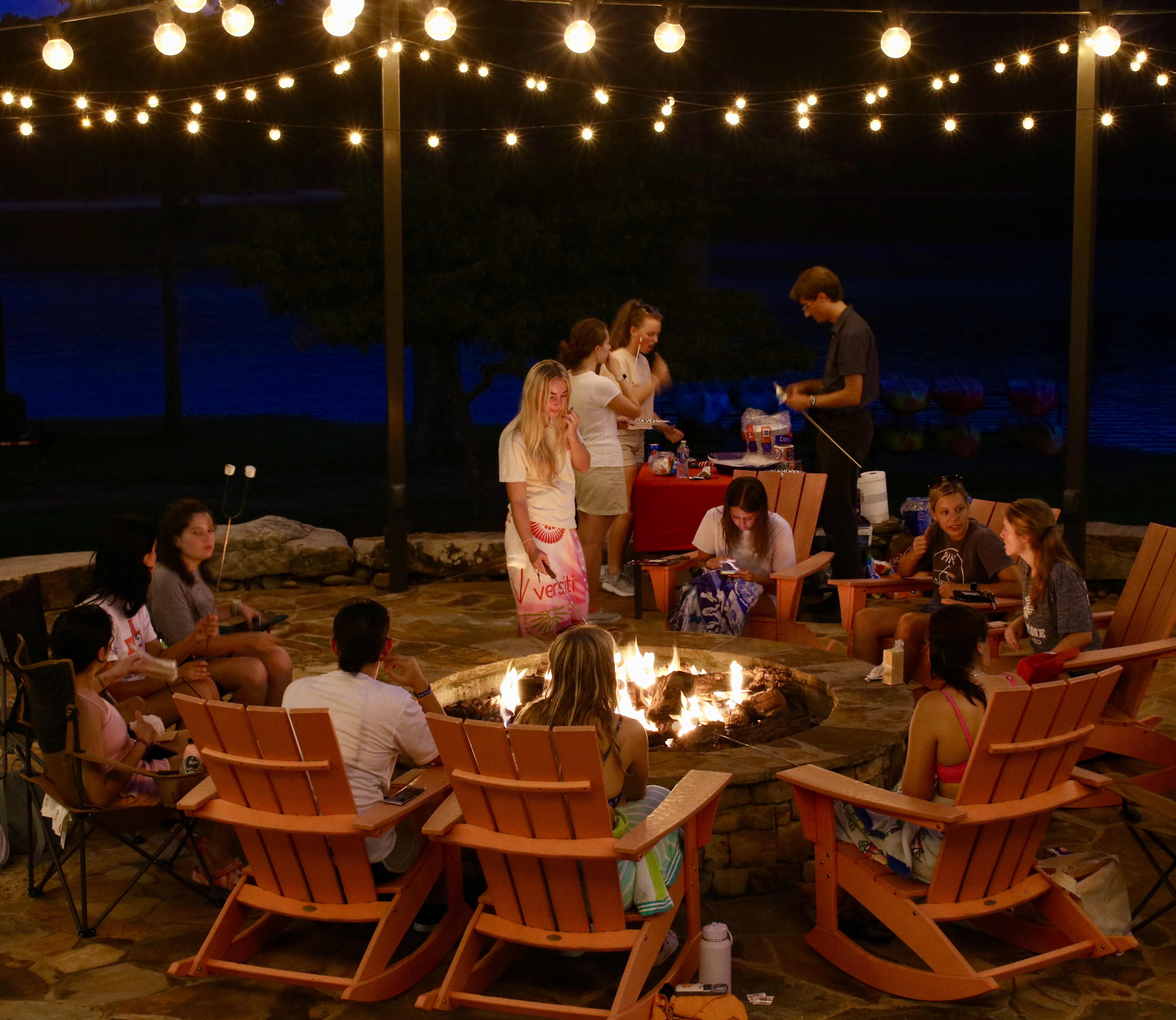 people sitting in orange rocking chairs roasting marshmellows around a stone firepit
