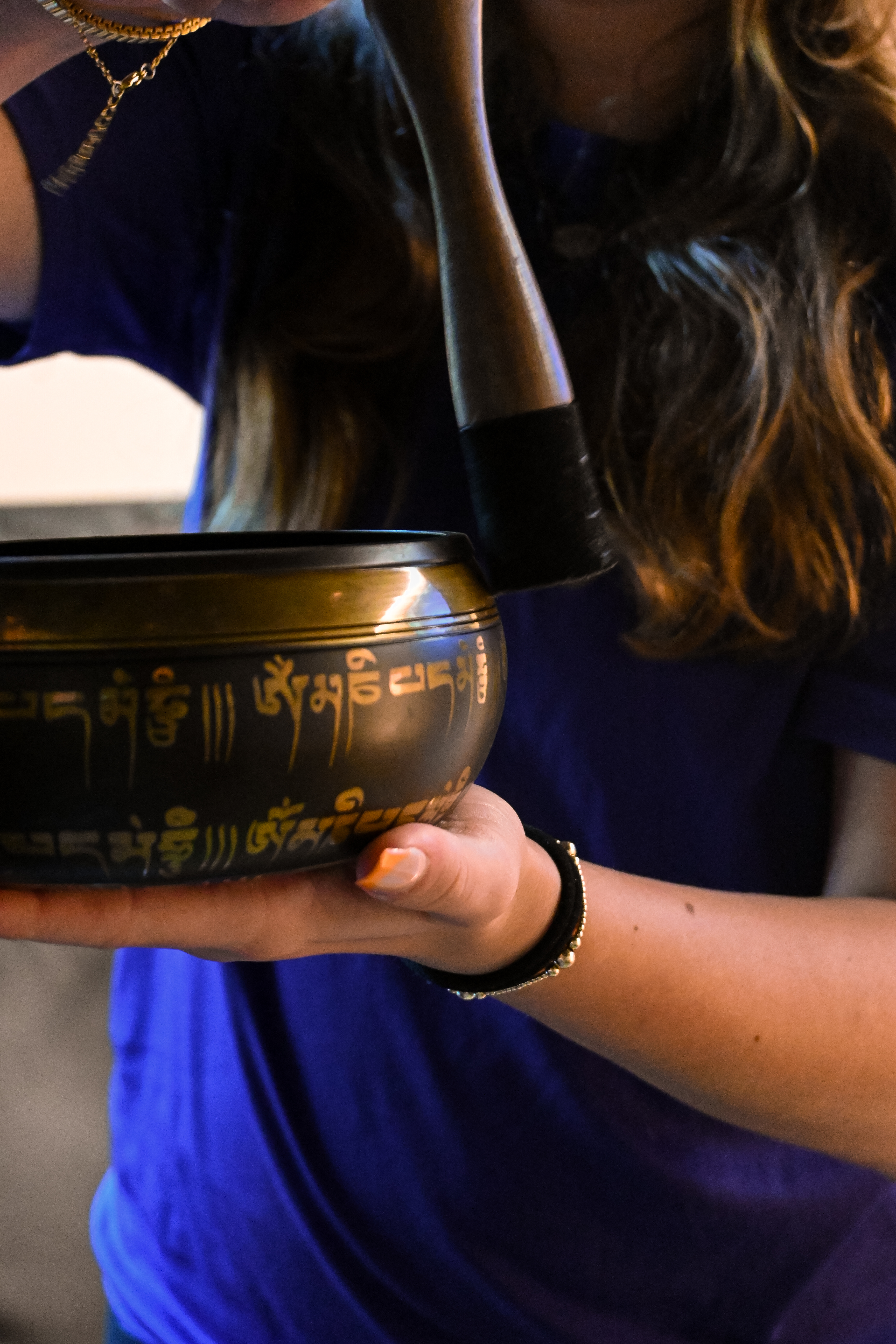 Person holding a Tibetan singing bowl with engraved symbols while striking it with a mallet.