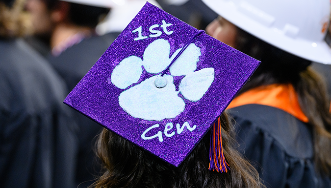 Clemson student wearing graduation cap decorated in purple sparkle with white Tiger Paw and 1st Gen written