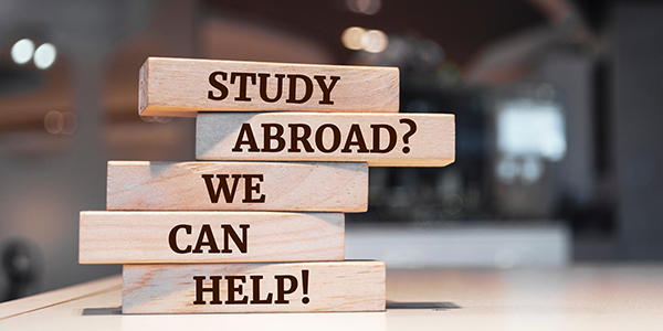 Wooden blocks stacked with the text "STUDY ABROAD? WE CAN HELP!" emphasizing support for students considering studying abroad.