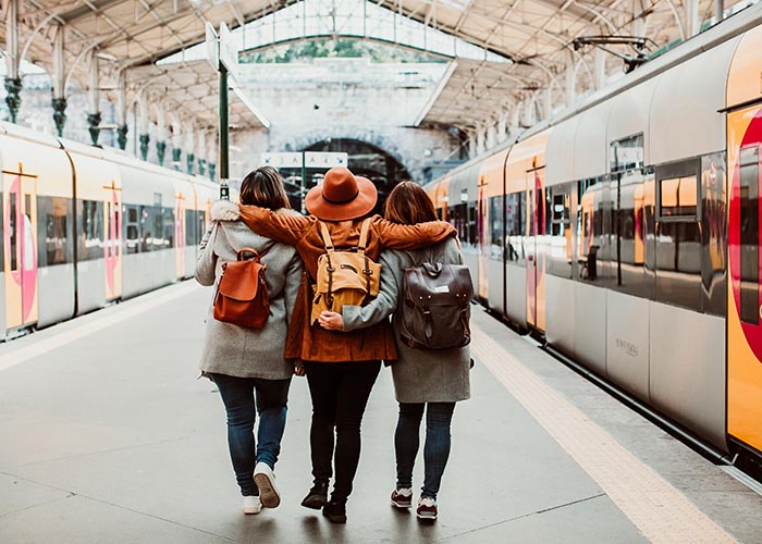 Three students arm in arm as they walk through a train station