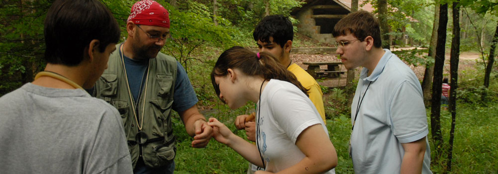 A camp counselor holds a small animal while campers gather around to observe