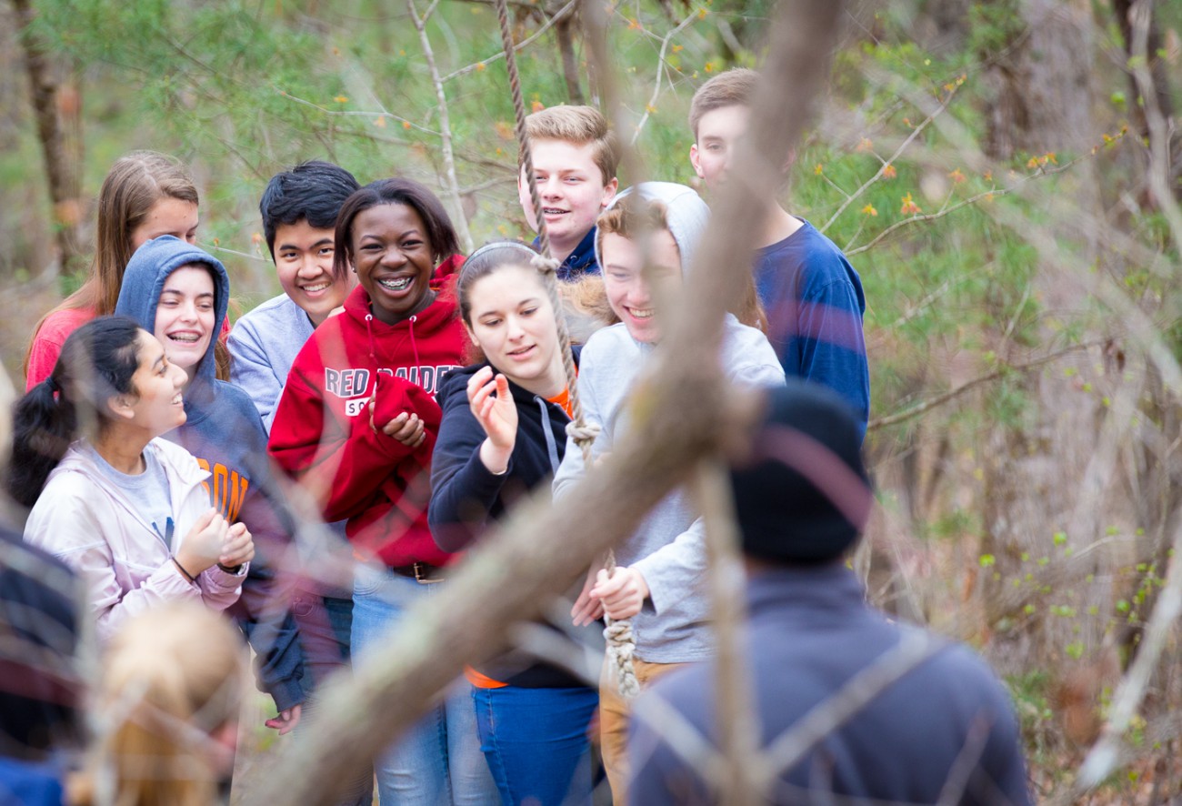 A group of campers gather near an activity in the woods