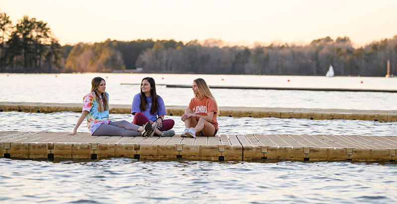 Three students sitting on a dock by Lake Hartwell