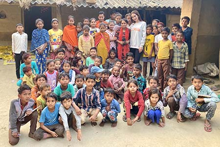 A Clemson student poses in a group picture with children in the center of a village.