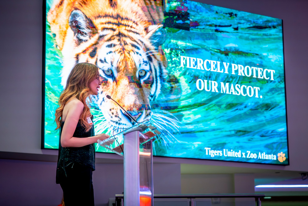 ssociate director Hrishita Negi speaking at a podium in front of a graphic of a tiger with the words 'fiercely protect our mascot'
