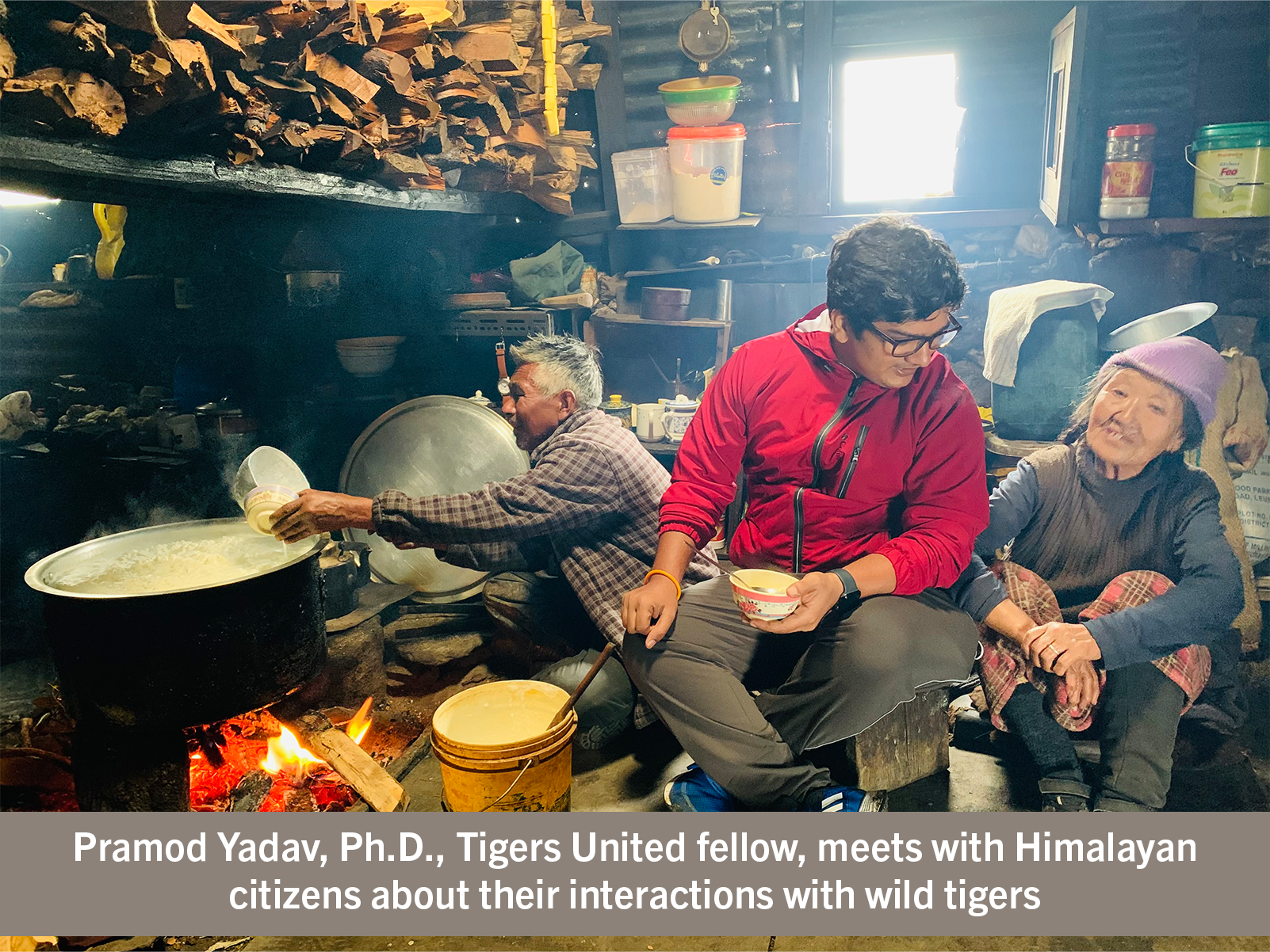 Three people sit near a fire to cook.