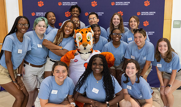 Group photo of students in light blue shirts with a tiger mascot in front of a Clemson University backdrop.