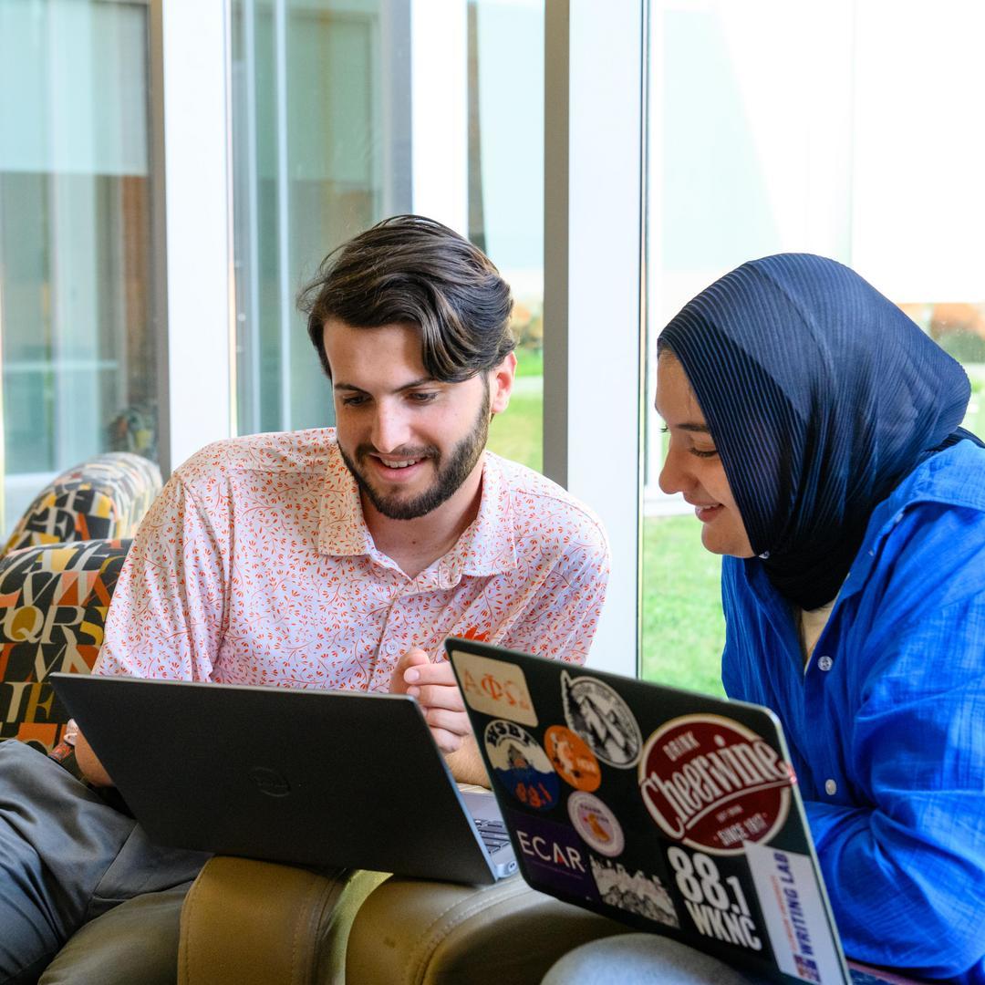 Male student engaging with female student in front of two laptops
