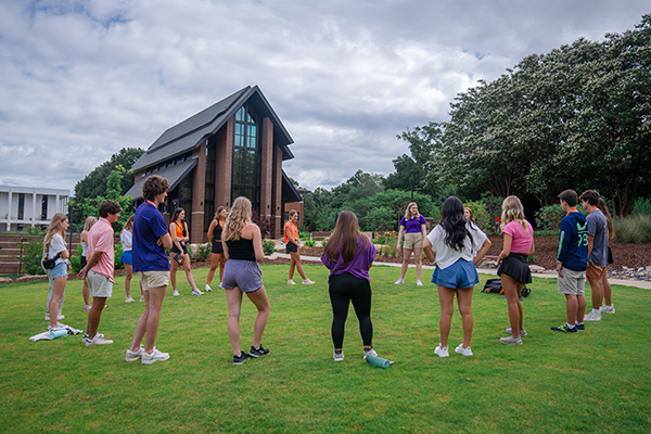Group of college students participating in an outdoor team-building activity on a grassy field near the Samuel J Cadden Chapel.