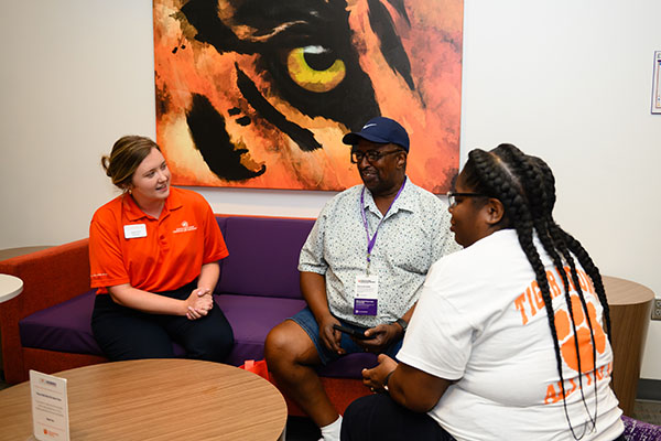 A staff member engages in conversation with two parents in a vibrant lounge area, featuring a striking tiger-themed artwork in the background.