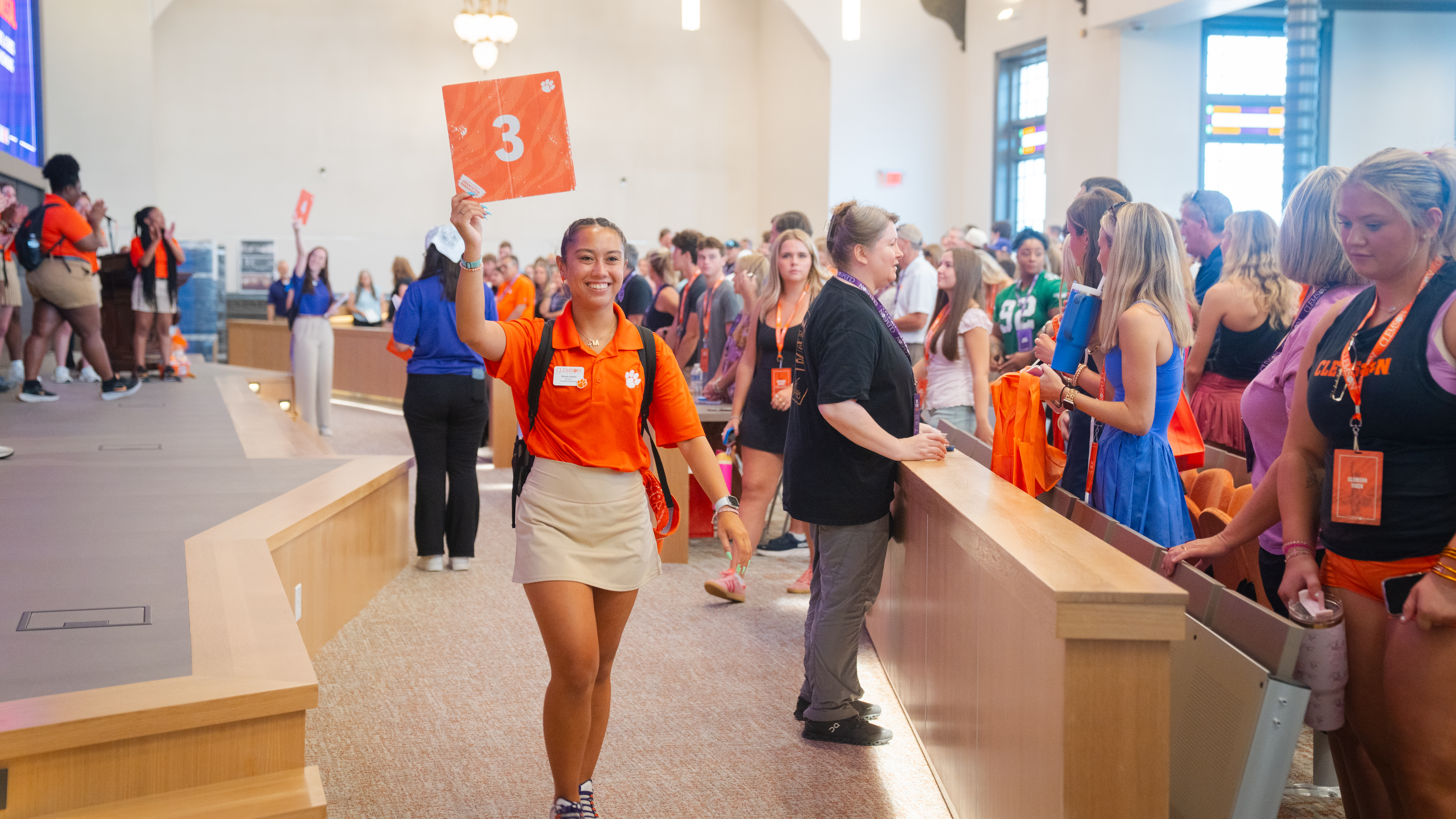 Student in orange polo holding orange card above head smiling