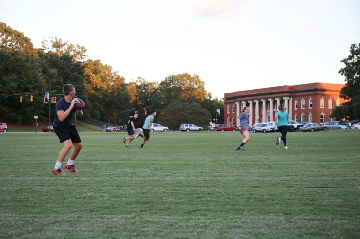 Students play football on bowman field out in front of Sikes Hall