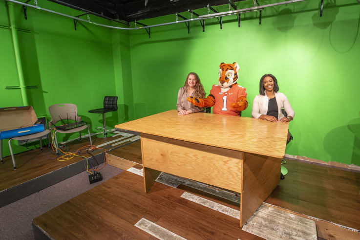 The Tiger and two students sit at a desk in theTiger Media and WYFF4 News Bureau