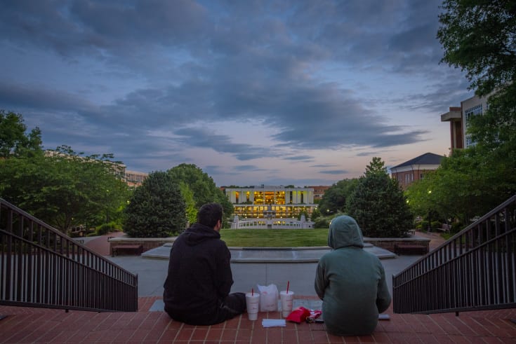 Two Students sit at the top of the north green facing the reflection pond