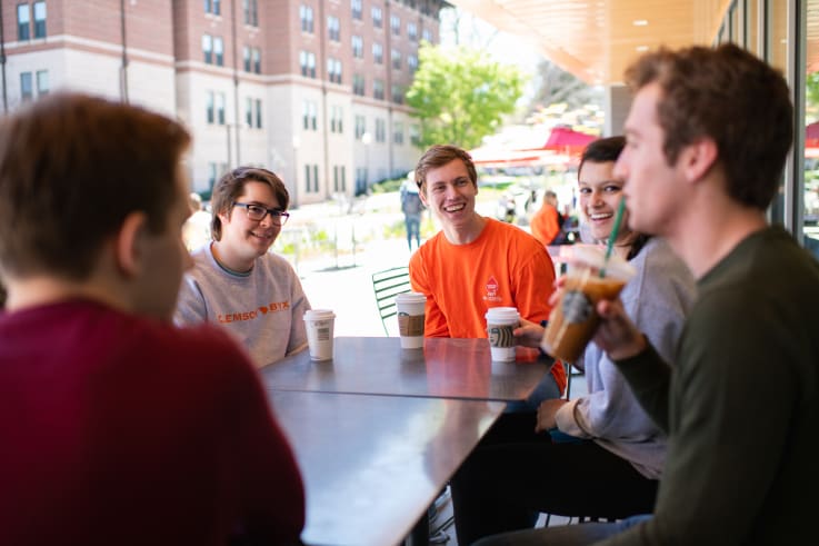 A group of students sit outside at a table in front of Deschamps hall