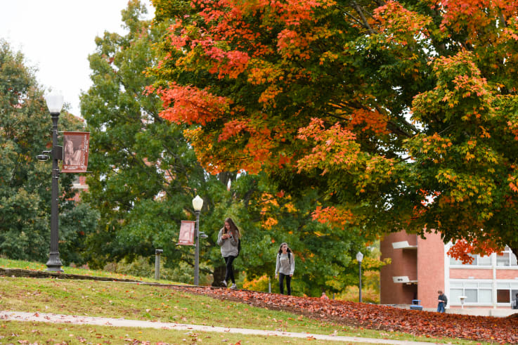 Two students walk along the sidewalk in front of the shoeboxes