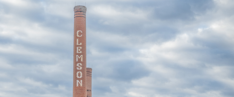 A brick smokestack with Clemson spelled out in bricks in front of clouds.