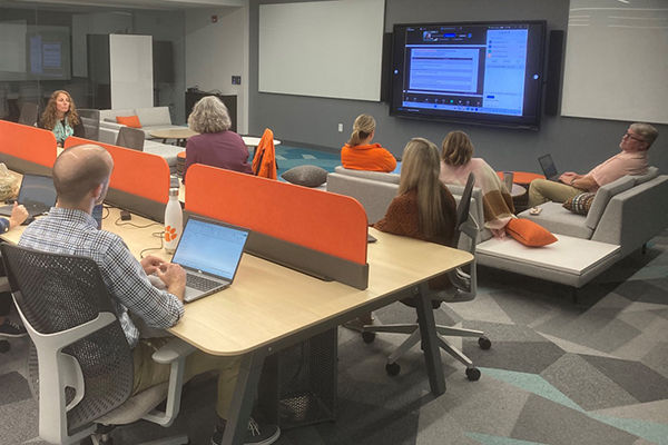 Conference room with large screen presentation and people discussing topics presented.